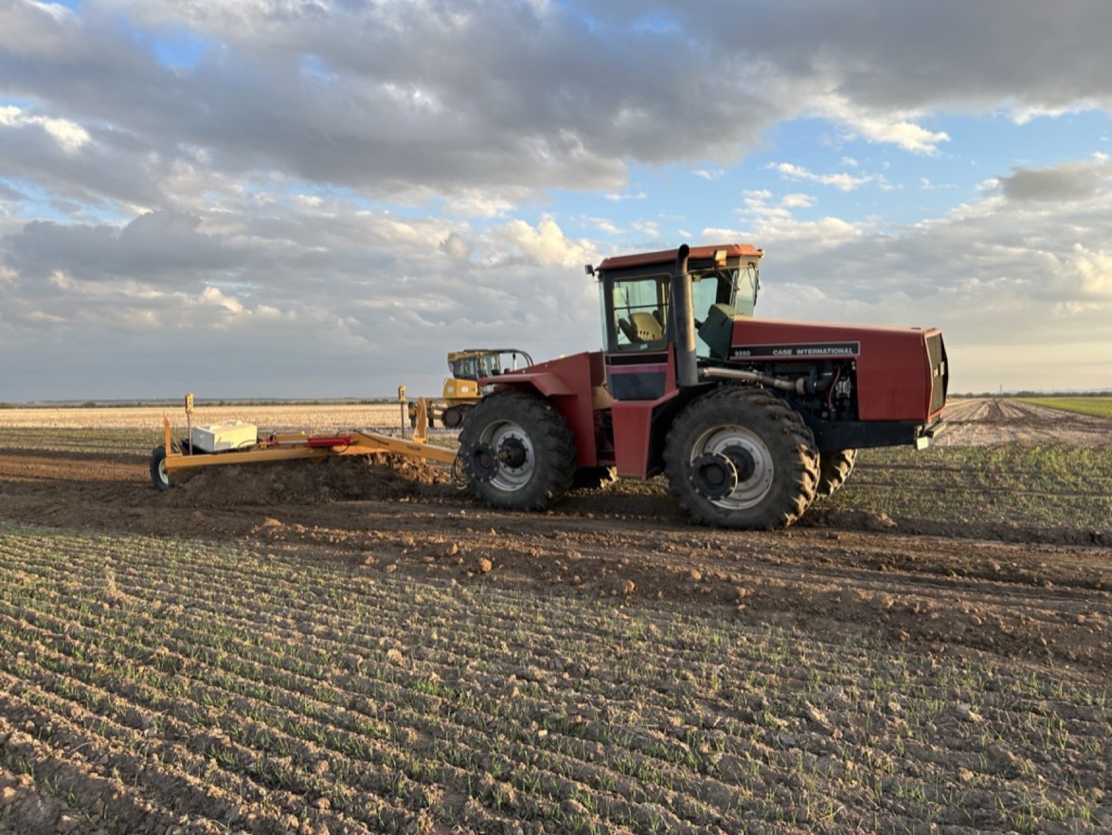 Tractor pulling a grading blade through a field
