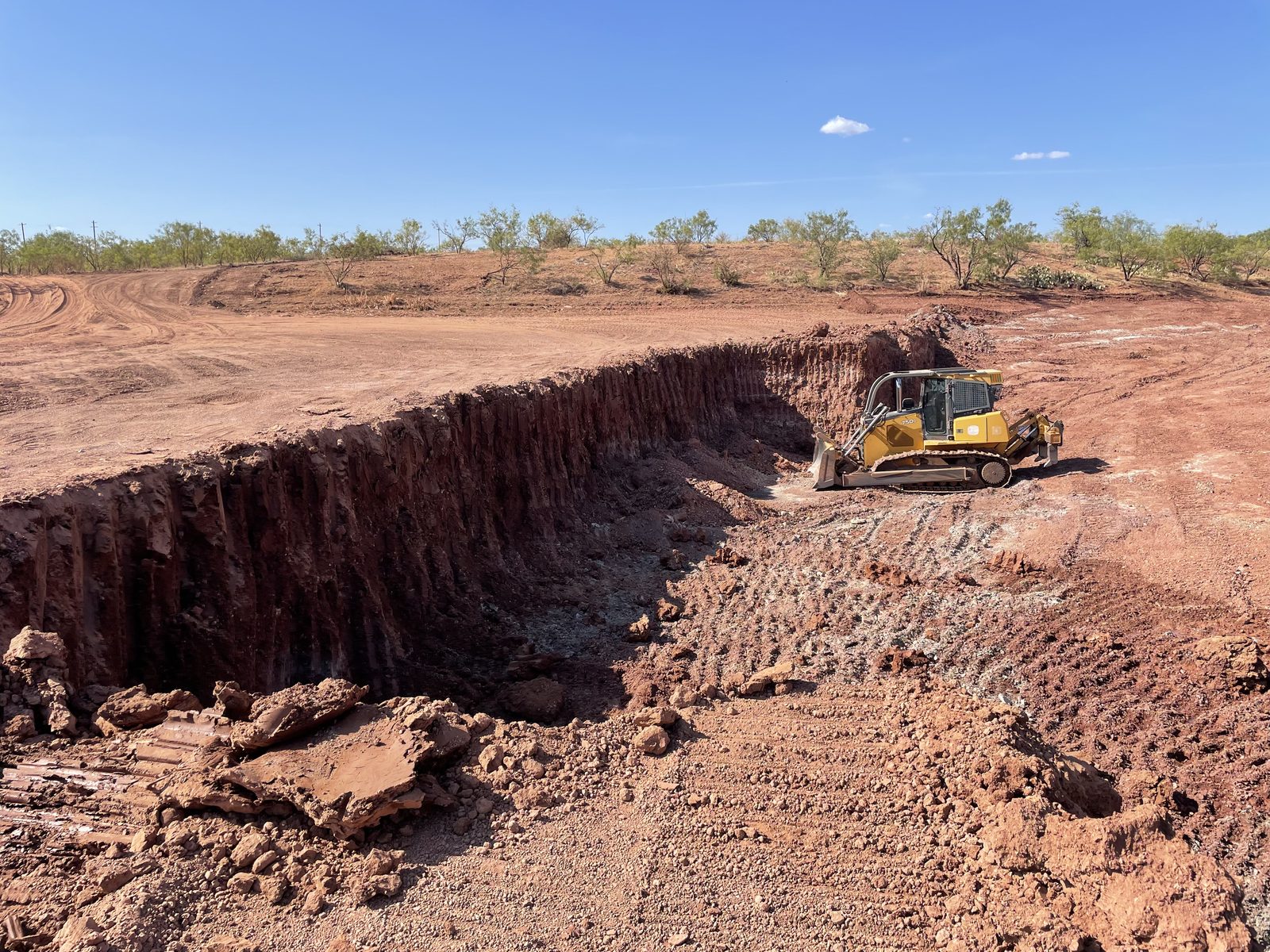 Pond under construction — red caliche banks, storm sky, Big Country Texas